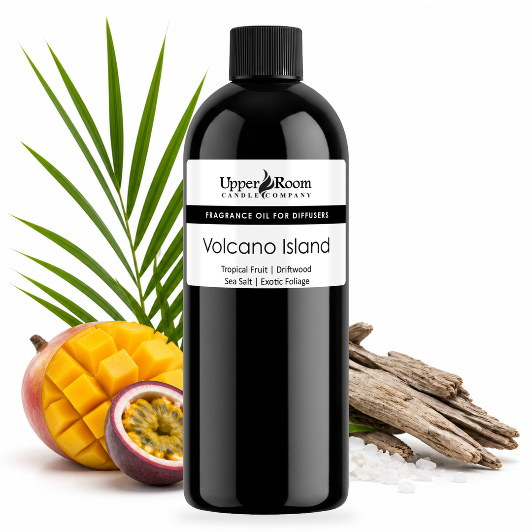 A black plastic bottle of Upper Room Candle Company Volcano Island fragrance oil for diffusers, styled with tropical ingredients including a sliced mango, a passion fruit, sea salt crystals, and driftwood on a white background.