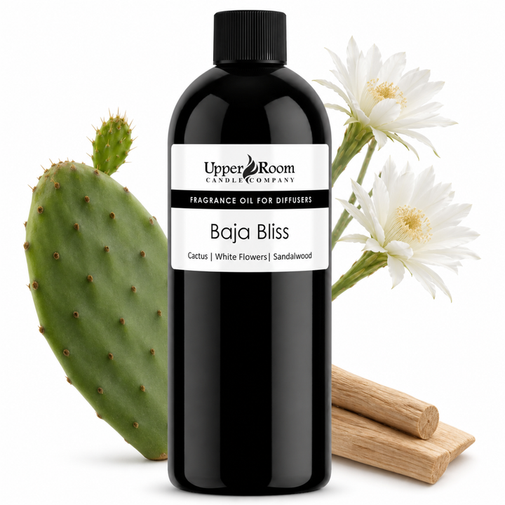 A black bottle of Upper Room Candle Company Baja Bliss fragrance oil for diffusers, styled with a green cactus, white flowers, and sandalwood sticks on a white background.