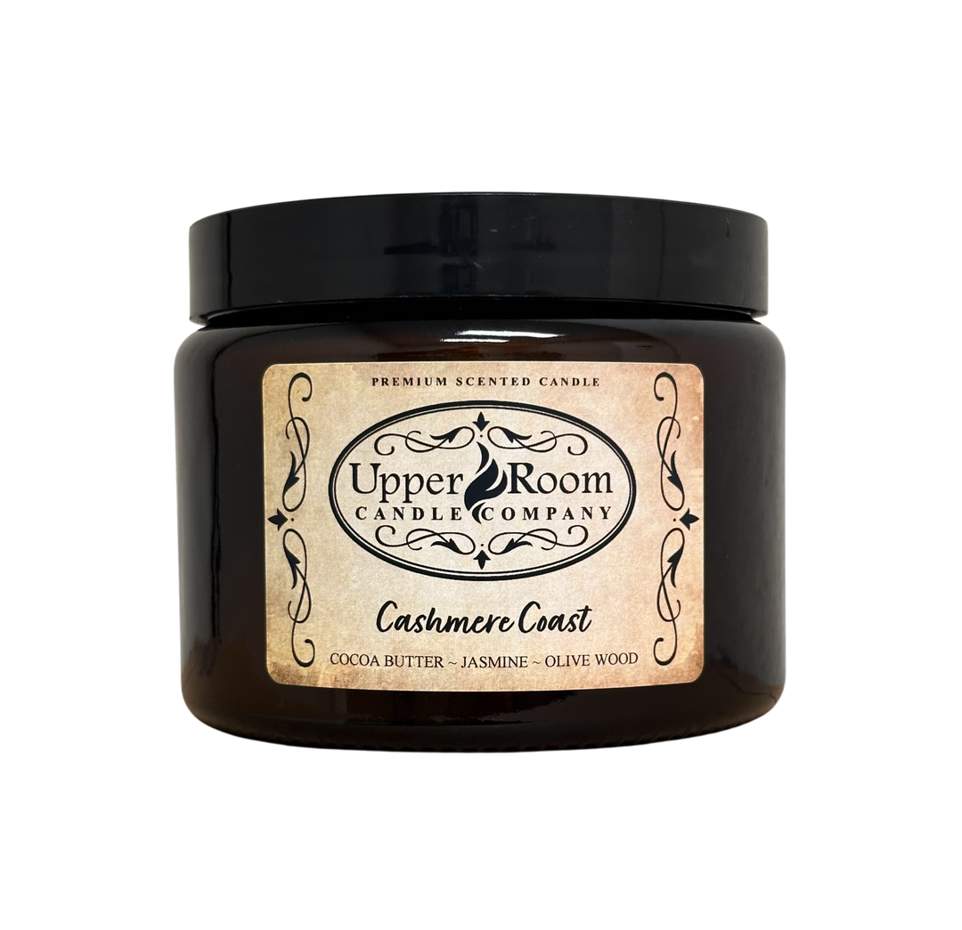 A Cashmere Coast candle jar, double wick amber jar with a label reading 'Upper Room Candle Company,  Cocoa Butter, Jasmine, Olive Wood'. 