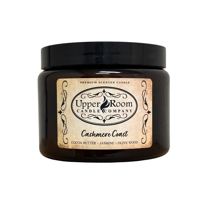 A Cashmere Coast candle jar, double wick amber jar with a label reading 'Upper Room Candle Company,  Cocoa Butter, Jasmine, Olive Wood'. 