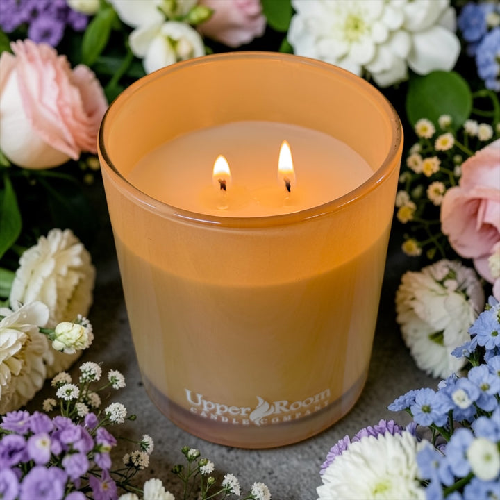 Amazing Grace Candle, Lit in a glass jar with 'Upper Room Candle Company' branding, surrounded by flowers.