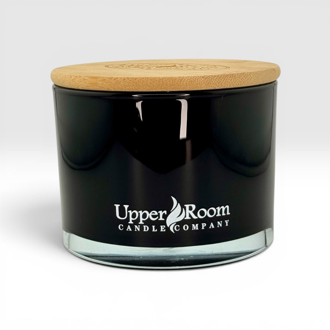 Black candle jar with wooden lid and 'Upper Room Candle Company' logo on a white background