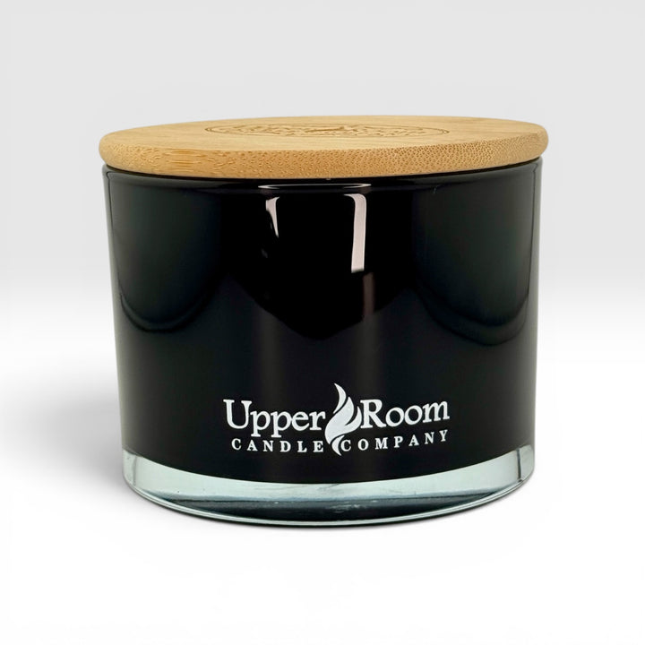 Black candle jar with wooden lid and 'Upper Room Candle Company' logo on a white background