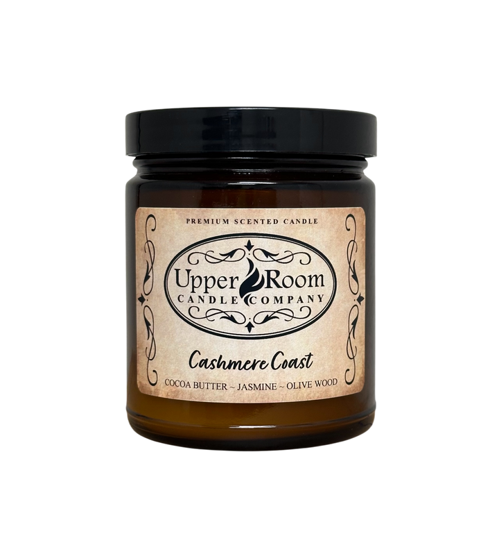A Cashmere Coast candle jar, single wick amber jar with a label reading 'Upper Room Candle Company,  Cocoa Butter, Jasmine, Olive Wood'. 