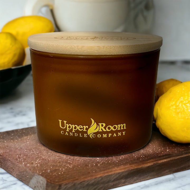 Lemon Pound Cake Candle, Triple Wick frosted amber jar on a cutting board surrounded by lemons, upper room candle company