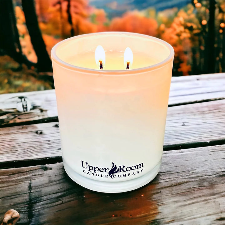 golden woods, double wick candle white jar, upper room candle, in front of an autumn forest 