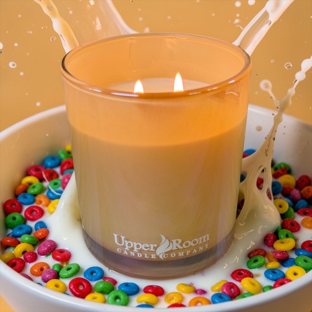 rainbow milk candle in a double wick gold jar from upper room candle company in a bowl of rainbow colored fruit cereal.