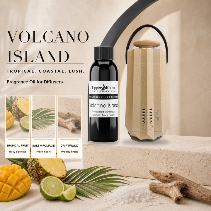 Volcano Island fragrance oil by Upper Room Candle Company shown with a black bottle and a beige diffuser, styled with tropical fruit, salt, wood, and palm leaves on a sandy surface. Text on the image reads 'VOLCANO ISLAND' and 'TROPICAL.